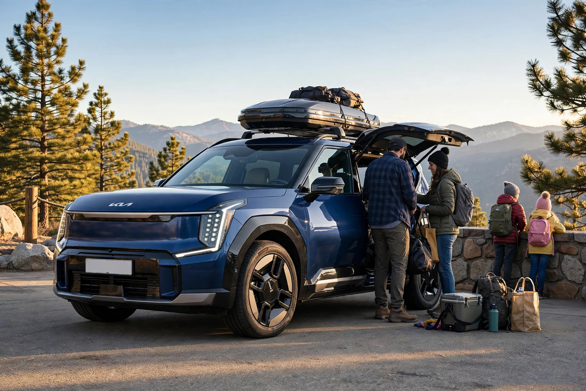 Kia EV9 deep blue three-row SUV with a roof box parked at a mountain overlook rest stop on a family road trip