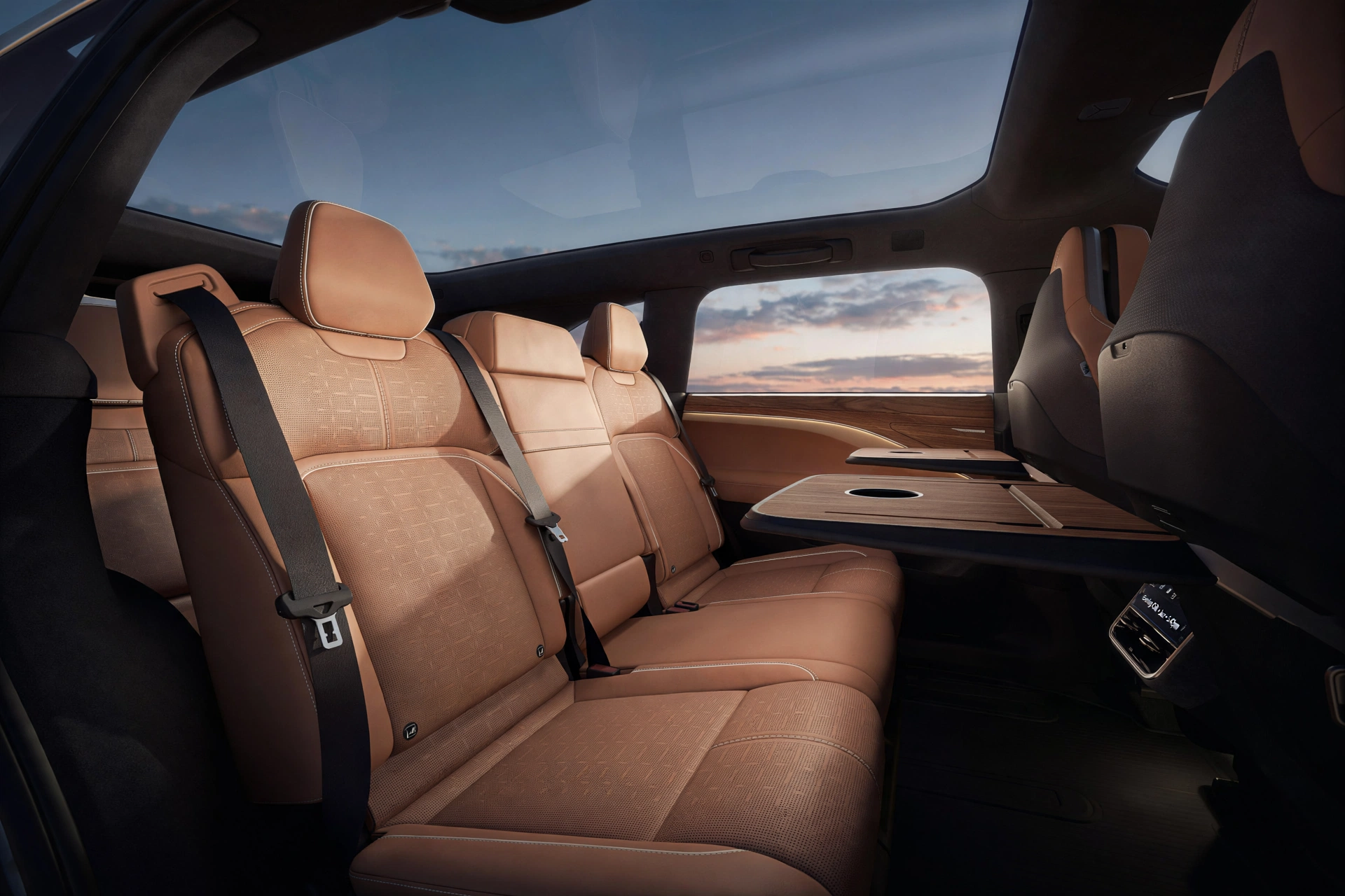 Second row of the Lucid Gravity with warm tan leather seats, wood-grain tray tables folded down and the glass roof overhead, the cabin detail that defines this lucid suv
